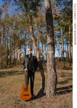 Blonde man playing string guitar outdoors in autumn forest. Concept of sound therapy, mental health and wellness rituals. Calmness tranquility audio-sensory practices. Aura farming energy Blonde man playing string guitar outdoors in autumn forest. Concept of sound therapy, mental health and wellness rituals. Calmness tranquility audio-sensory practices. Aura farming energy 139471721