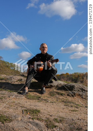 Blonde man playing string guitar outdoors in autumn forest. Concept of sound therapy, mental health and wellness rituals. Calmness tranquility audio-sensory practices. Aura farming energy Blonde man playing string guitar outdoors in autumn forest. Concept of sound therapy, mental health and wellness rituals. Calmness tranquility audio-sensory practices. Aura farming energy 139471729