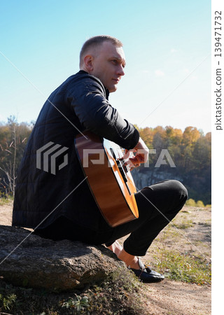 Blonde man playing string guitar outdoors in autumn forest. Concept of sound therapy, mental health and wellness rituals. Calmness tranquility audio-sensory practices. Aura farming energy Blonde man playing string guitar outdoors in autumn forest. Concept of sound therapy, mental health and wellness rituals. Calmness tranquility audio-sensory practices. Aura farming energy 139471732