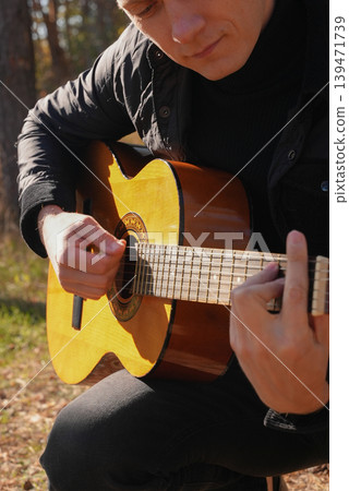 Portrait of smiling caucasian artist plays wooden acoustic guitar in autumnal park. Young songwriter plays string musical instrument hobby outside in nature fall time. Audio music healing 139471739