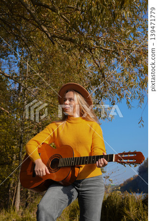Beautiful blonde girl playing acoustic guitar and singing relaxing enjoying outdoors on sunny autumn day. Hippie woman in boho style learning and practicing playing musical instrument. Fall leaves Beautiful blonde girl playing acoustic guitar and singing relaxing enjoying outdoors on sunny autumn day. Hippie woman in boho style learning and practicing playing musical instrument. Fall leaves 139471779