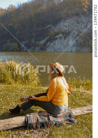 Beautiful blonde girl playing acoustic guitar and singing relaxing enjoying outdoors on sunny autumn day. Hippie woman in boho style learning and practicing playing musical instrument. Fall leaves Beautiful blonde girl playing acoustic guitar and singing relaxing enjoying outdoors on sunny autumn day. Hippie woman in boho style learning and practicing playing musical instrument. Fall leaves 139471782