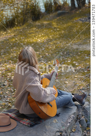 Portrait of smiling caucasian artist plays wooden acoustic guitar in autumnal park. Young songwriter plays string musical instrument hobby outside in nature fall time. Audio music healing Portrait of smiling caucasian artist plays wooden acoustic guitar in autumnal park. Young songwriter plays string musical instrument hobby outside in nature fall time. Audio music healing 139471783