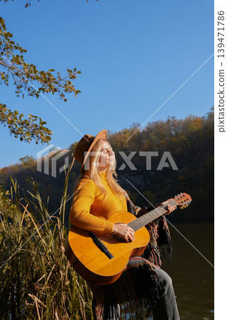 Portrait of smiling caucasian artist plays wooden acoustic guitar in autumnal park. Young songwriter plays string musical instrument hobby outside in nature fall time. Audio music healing Portrait of smiling caucasian artist plays wooden acoustic guitar in autumnal park. Young songwriter plays string musical instrument hobby outside in nature fall time. Audio music healing 139471786