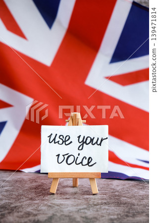 Paper note with words USE YOUR VOICE on National symbol of Great Britain. British wave the UK silky flag background. Ellection political participation campaign and civic engagement Paper note with words USE YOUR VOICE on National symbol of Great Britain. British wave the UK silky flag background. Ellection political participation campaign and civic engagement 139471814