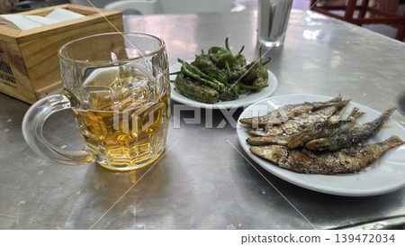 Glass of beer with fried anchovies and padron peppers on metal table for spanish tapas food background and casual restaurant scene Glass of beer with fried anchovies and padron peppers on metal table for spanish tapas food background and casual restaurant scene 139472034