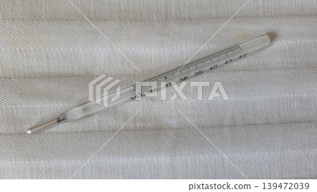 Glass mercury clinical thermometer on textured fabric background for medical illustration and health banner design Glass mercury clinical thermometer on textured fabric background for medical illustration and health banner design 139472039