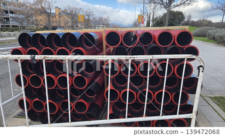 Stacks of red drainage pipes behind safety barriers for road repair background and construction site banner Stacks of red drainage pipes behind safety barriers for road repair background and construction site banner 139472068