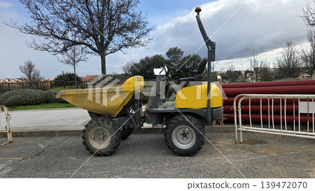 Mini dumper parked beside red drainage pipes and barriers for construction site equipment showcase and maintenance background Mini dumper parked beside red drainage pipes and barriers for construction site equipment showcase and maintenance background 139472070