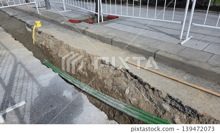 Open utility trench with green conduit pipes along sidewalk for road repair and pipe laying infrastructure background Open utility trench with green conduit pipes along sidewalk for road repair and pipe laying infrastructure background 139472073