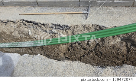 Closeup green conduit cables in roadside trench with hand rake for pipe laying and utility repair background. Telecommunication pipes Closeup green conduit cables in roadside trench with hand rake for pipe laying and utility repair background. Telecommunication pipes 139472074
