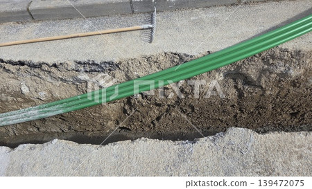 Green conduit in roadside trench for road repair and pipe laying background for infrastructure construction project. Telecommunication pipes 139472075