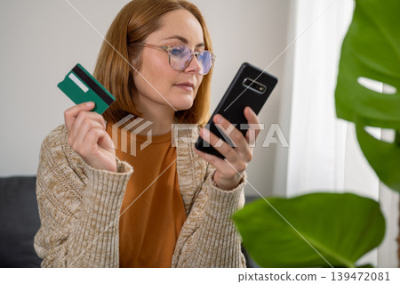 Woman holding smart phone and credit card at home, sitting on the sofa Woman holding smart phone and credit card at home, sitting on the sofa 139472081