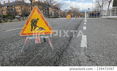 Closeup roadwork warning sign on fractured asphalt with twenty speed sign for urban street repair background and maintenance notice Closeup roadwork warning sign on fractured asphalt with twenty speed sign for urban street repair background and maintenance notice 139472097