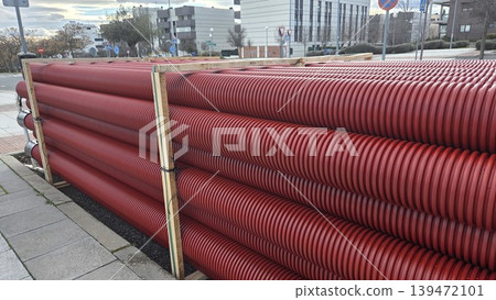 Long rows of red corrugated drainage pipes strapped in wooden frames for road repair and public works supply background and construction banner Long rows of red corrugated drainage pipes strapped in wooden frames for road repair and public works supply background and construction banner 139472101