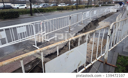 Long urban roadside trench for pipe laying and road repair with metal barriers and traffic control for infrastructure maintenance and documentation background 139472107