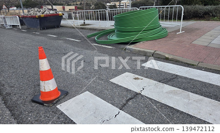 Utility pipe coil and traffic cones at pedestrian zebra crossing with safety barriers for road repair and pipe laying background for municipal construction design 139472112