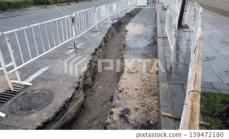 Open roadside trench and excavated sidewalk area for utility repair and pipe laying background for construction signage Open roadside trench and excavated sidewalk area for utility repair and pipe laying background for construction signage 139472180