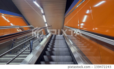 Escalator leading up through modern madrid metro station with orange tiled walls and stainless steel handrails for transport background and architecture poster Escalator leading up through modern madrid metro station with orange tiled walls and stainless steel handrails for transport background and architecture poster 139472243