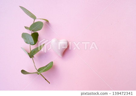 A heartshaped stone surrounded by green leaves set against a soft pink background creates a serene atmosphere A heartshaped stone surrounded by green leaves set against a soft pink background creates a serene atmosphere 139472341