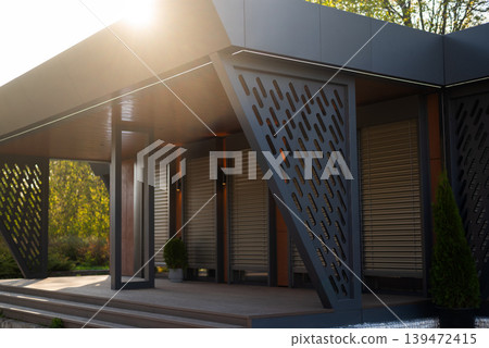 Modern luxury modular house with terrace, anthracite metal panels, wooden details, and automatic shutters at sunset. Modern luxury modular house with terrace, anthracite metal panels, wooden details, and automatic shutters at sunset. 139472415