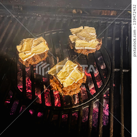 uicy beef burger patties cooking on a hot barbecue grill with melting brie cheese over glowing charcoal. Rustic outdoor grilling scene with smoky atmosphere and comfort food styling uicy beef burger patties cooking on a hot barbecue grill with melting brie cheese over glowing charcoal. Rustic outdoor grilling scene with smoky atmosphere and comfort food styling 139472432