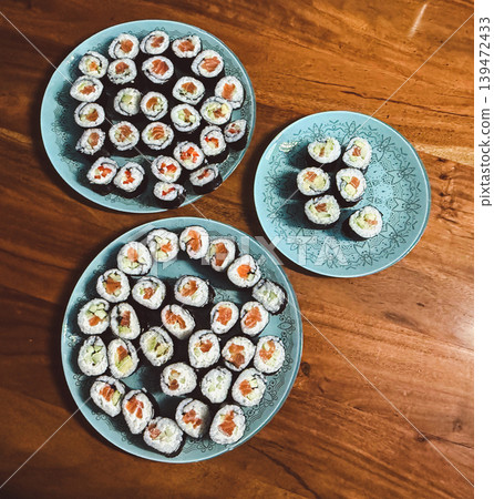 Assorted homemade sushi rolls with salmon and avocado served on decorative plates over a wooden table. Japanese inspired dinner composition with rustic homemade atmosphere Assorted homemade sushi rolls with salmon and avocado served on decorative plates over a wooden table. Japanese inspired dinner composition with rustic homemade atmosphere 139472433