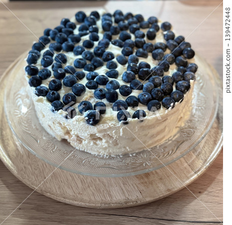 Rustic homemade blueberry cream cake on a glass serving plate with fresh berries and soft natural light. Trendy cozy food photography with bakery inspired aesthetic Rustic homemade blueberry cream cake on a glass serving plate with fresh berries and soft natural light. Trendy cozy food photography with bakery inspired aesthetic 139472448
