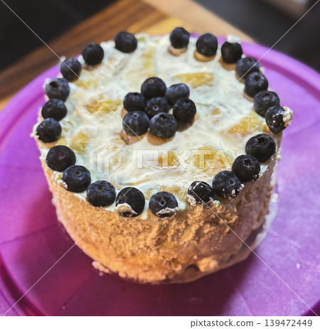 Fresh homemade sponge cake with creamy frosting and juicy blueberries on top. Cozy aesthetic dessert photography with soft focus and bakery style mood 139472449