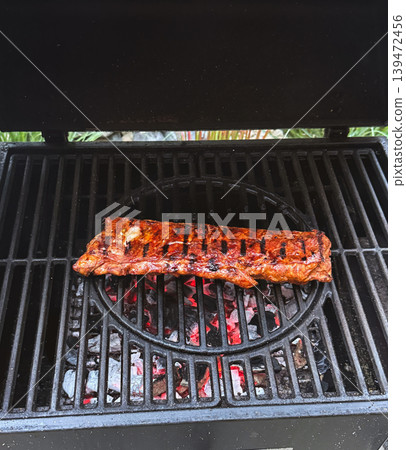 Juicy pork ribs grilling over glowing charcoal on an open barbecue with visible heat and smoke. Rustic outdoor cooking atmosphere 139472456