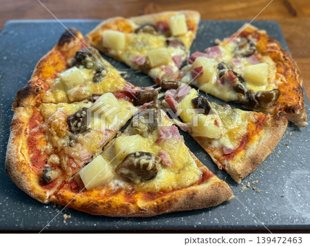 Homemade pizza with pineapple ham and mushrooms on a rustic board. Warm baked cheese creates an inviting comfort food mood 139472463