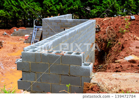 Workers are building concrete block wall on construction site with dirt tools nearby. Workers are building concrete block wall on construction site with dirt tools nearby. 139472784