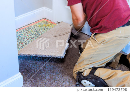 Worker kneels on floor, removes pulling up carpet to prepare for new flooring in house. Worker kneels on floor, removes pulling up carpet to prepare for new flooring in house. 139472798