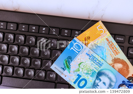 New Zealand currency cash notes lay on computer keyboard in an office while may be working studying. New Zealand currency cash notes lay on computer keyboard in an office while may be working studying. 139472809