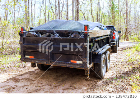 Dump trailer to garbage is parked on dirt road surrounded by trees Dump trailer to garbage is parked on dirt road surrounded by trees 139472810