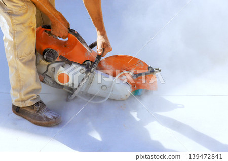 Worker operated concrete saw to cut surface at site while dust clouds form around area from action. Worker operated concrete saw to cut surface at site while dust clouds form around area from action. 139472841