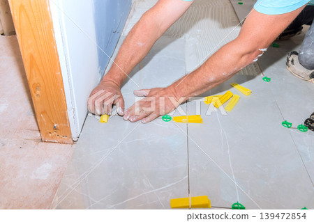 Tiler worker lays tiles on floor using spacers tools in construction setting Tiler worker lays tiles on floor using spacers tools in construction setting 139472854