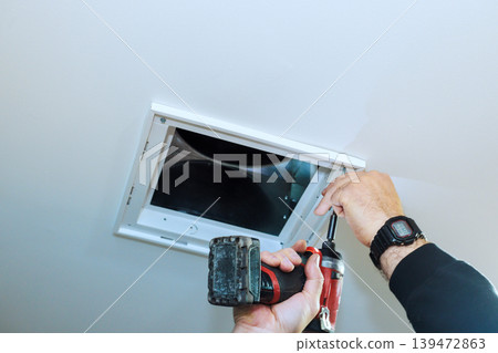 Worker is fixing ceiling vent using power drill screwdriver in house setting. Worker is fixing ceiling vent using power drill screwdriver in house setting. 139472863