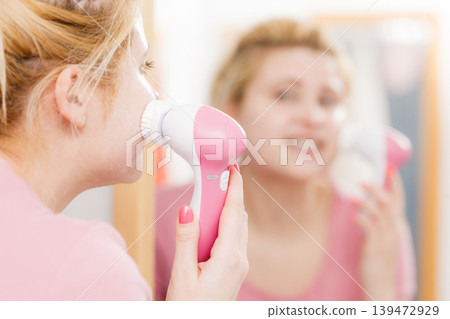 Happy woman using facial cleansing brush Happy woman using facial cleansing brush 139472929