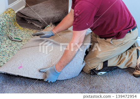 Worker kneels, pulls up an old carpet to prepare floor for new installation in house. Worker kneels, pulls up an old carpet to prepare floor for new installation in house. 139472954