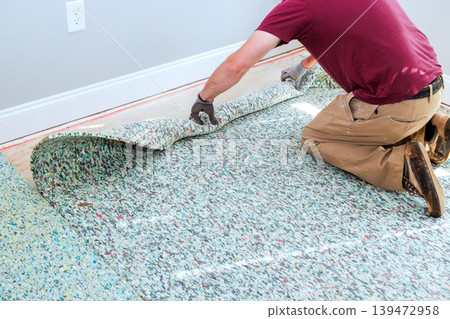 Worker pulls up piece of old carpet in room with light walls wood floor. Worker pulls up piece of old carpet in room with light walls wood floor. 139472958