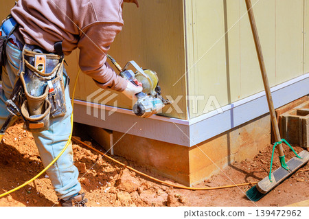 Worker using nail gun to attach panels on building site to materials to foundation Worker using nail gun to attach panels on building site to materials to foundation 139472962