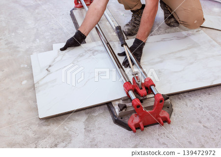 Worker cuts marble tiles using tile cutter during home renovation in building space. Worker cuts marble tiles using tile cutter during home renovation in building space. 139472972