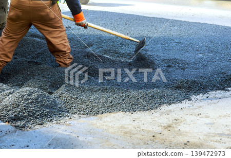 Worker uses tool to distribute asphalt on road surface in busy city area Worker uses tool to distribute asphalt on road surface in busy city area 139472973
