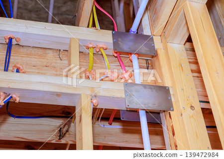 Workers install water pipes, electrical wires in building under construction with wooden beams, metal plates. 139472984