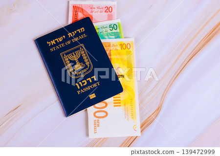 Passport from Israel lies flat with new Israeli shekel NIS banknotes nearby on white surface. Passport from Israel lies flat with new Israeli shekel NIS banknotes nearby on white surface. 139472999