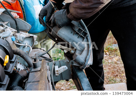 Worker are working on car headlight one is removing part while others observe assist in garage. Worker are working on car headlight one is removing part while others observe assist in garage. 139473004