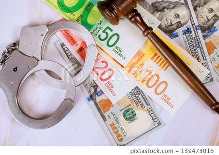 Handcuffs on various new Israeli shekels banknotes, law gavel used in court for legal matters involving money. Handcuffs on various new Israeli shekels banknotes, law gavel used in court for legal matters involving money. 139473016