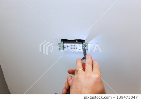 Handyman is installing an electrical outlet in wall they are using screwdriver to secure it in place Handyman is installing an electrical outlet in wall they are using screwdriver to secure it in place 139473047
