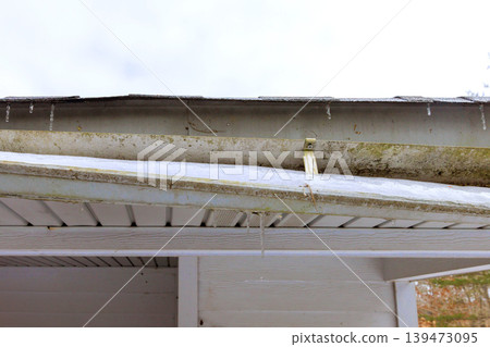 Snow collects on edge of roof, while icicles hang from damaged gutter Snow collects on edge of roof, while icicles hang from damaged gutter 139473095